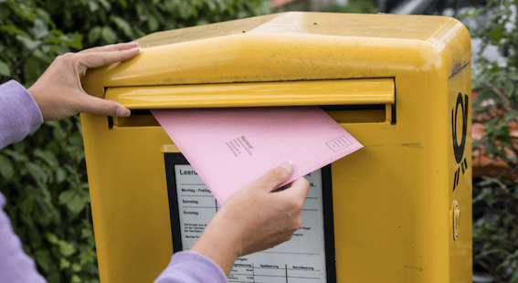 Eine Person wirft einen Briefwahl-Umschlag in einen Briefkasten.