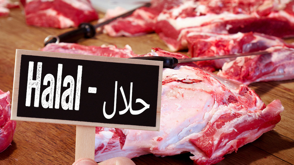 Fleisch auf einem Holzbrett, davor ein Schild auf dem Halal steht